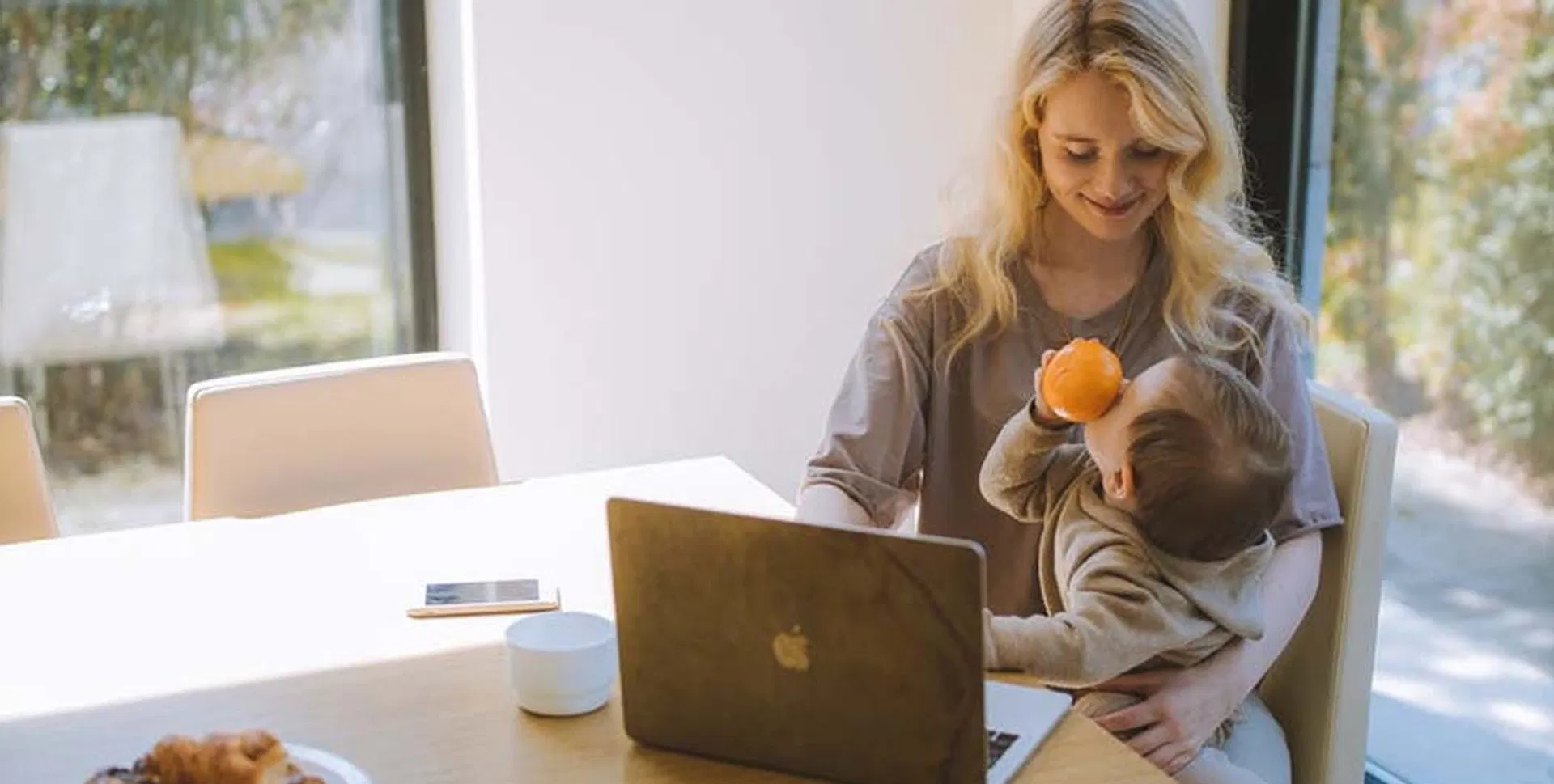 Edullisen lainan löytänyt äiti istuu hymyillen tietokoneen äärellä pieni lapsi sylissään