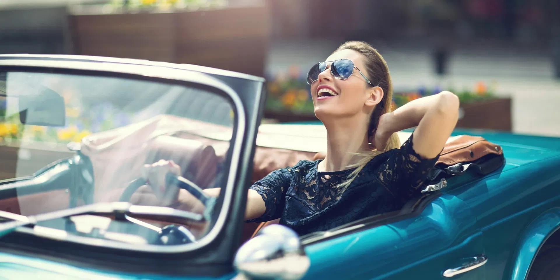 Nainen aurinkolaseissa hymyilee avoauton ratissa