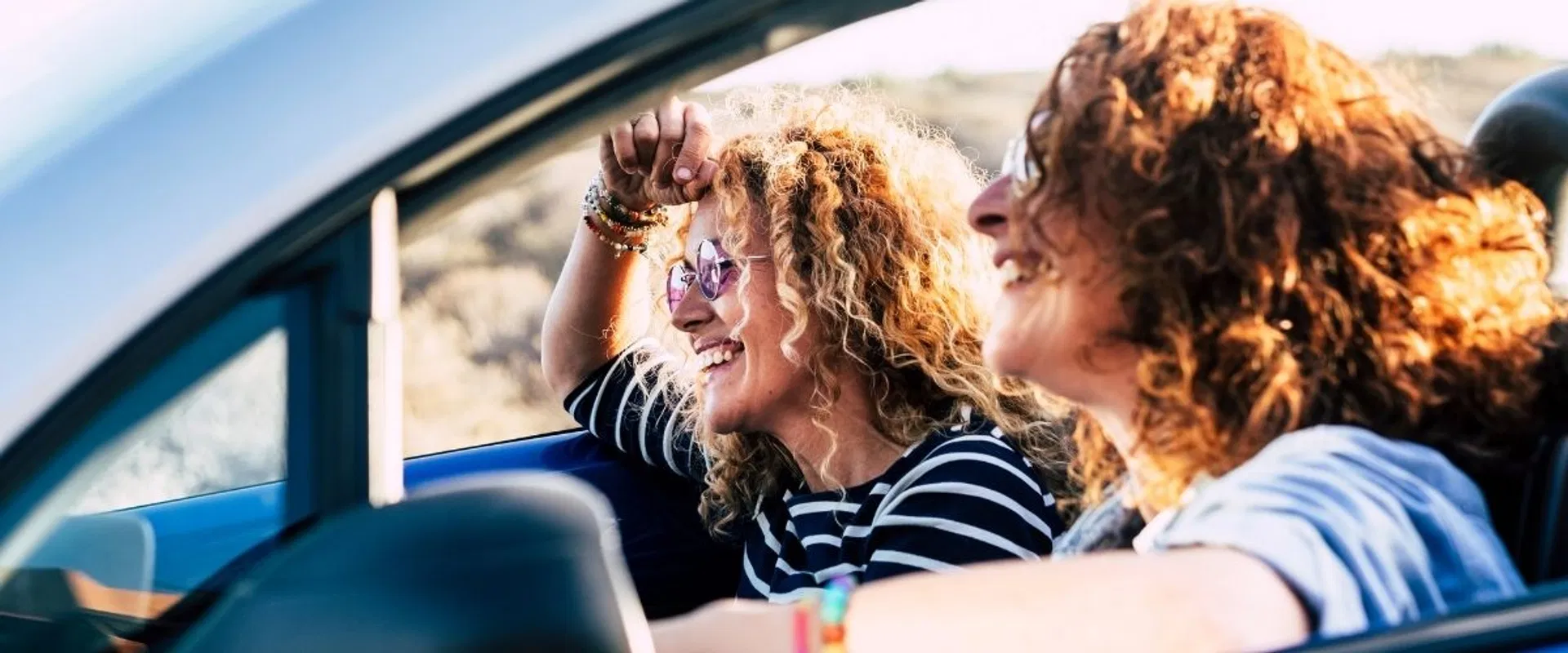 Kaksi iloista kiharahiuksista naista ajaa avoautolla ja nauttivat huolettomasta elämästä yhdistettyään kalliit lainansa.